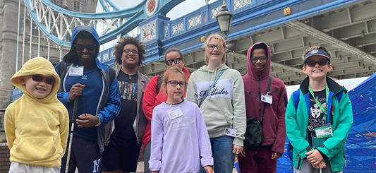 A group of young people of different ages stand together at Tower Bridge after their Horrible Histories boat trip. They're smiling happily.
