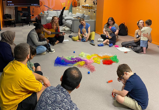 A group of parents and young children sit on the floor in a circle around colourful toys at RSBC's Life Without Limits Centre