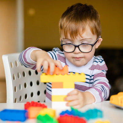 a young boy with glasses playing with colourful Duplo blocks