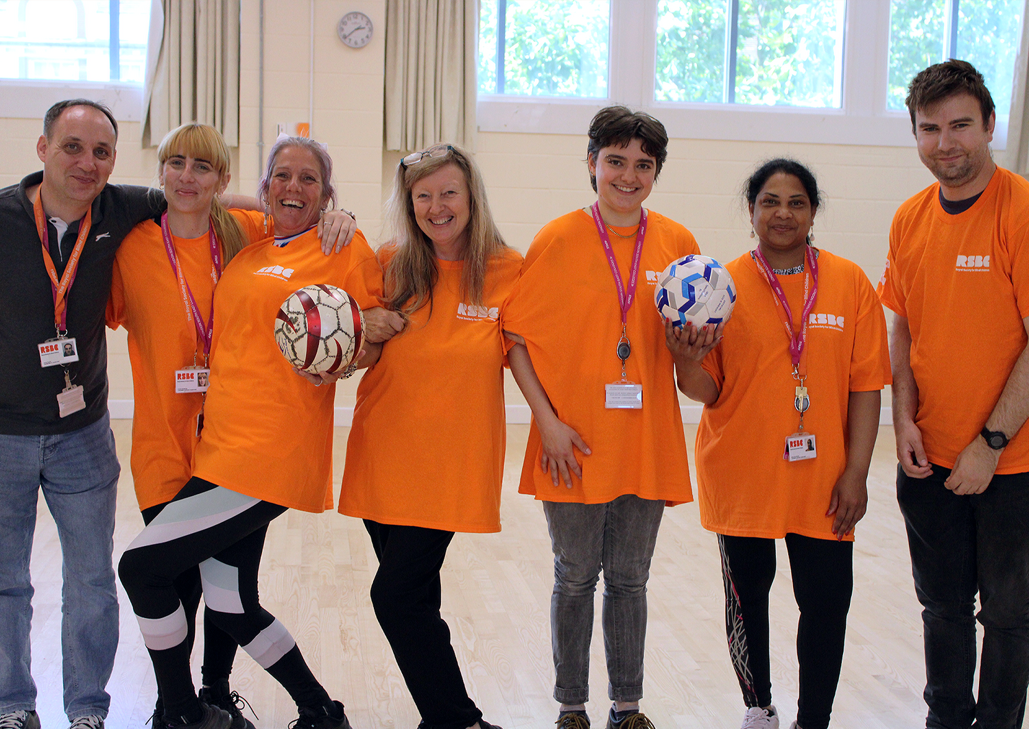 A beaming group of Dorton College LSAs holding footballs in a gymnasium