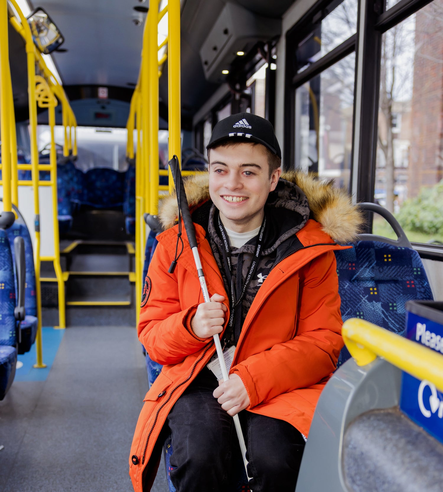 A young man with a cane smiling as he is sat on a bus, travelling independently