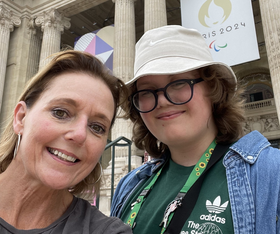 Raffy and his mother posing in front of a historic building with tall columns and a Paris 2024 Olympic banner in the background.
