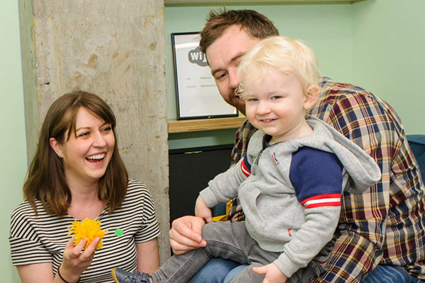 A family sitting in a room with a boy on the lap of his father.