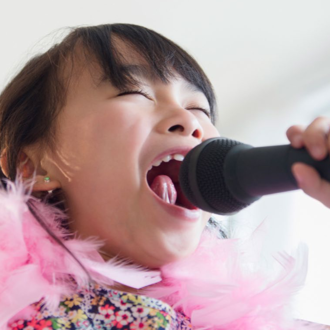 A young girl wearing a big pink feather boa and singing loudly into a microphone