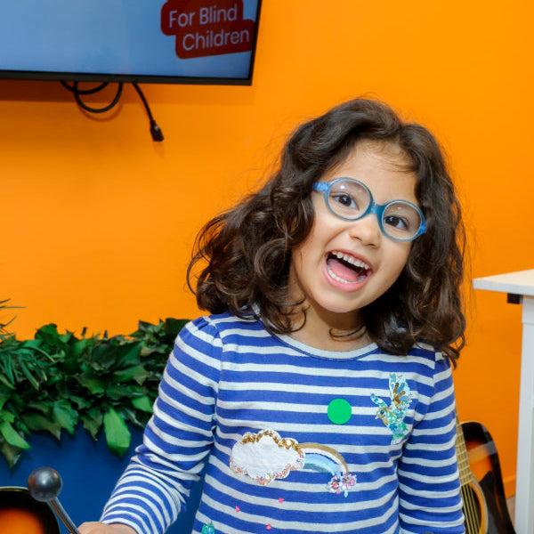 A happy young girl with glasses smiling in a brightly coloured room playing a xylophone