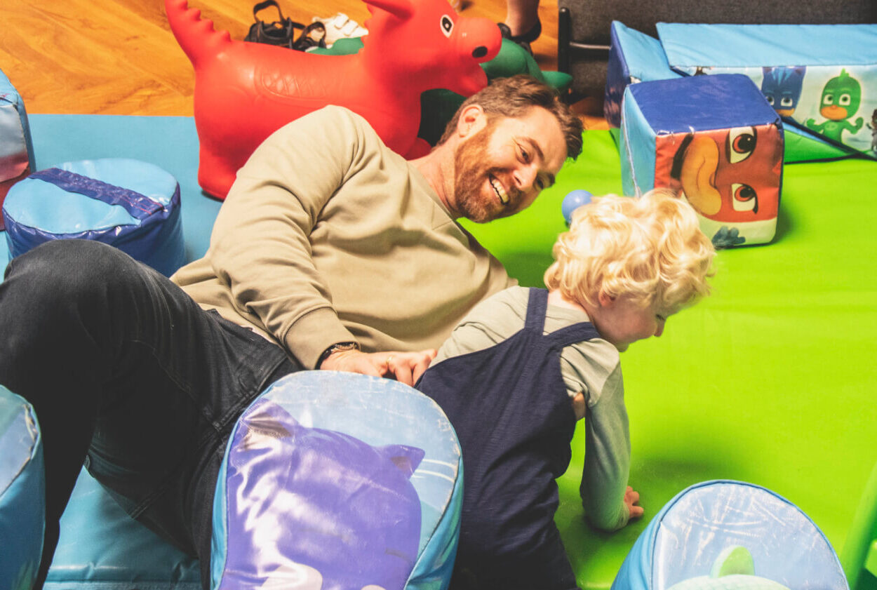 A dad and a young boy are rolling around having a brilliant time in a colourful soft play