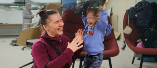 A mum laughs joyfully as her little boy playfully wafts a silk scarf over his head at a sensory play session.
