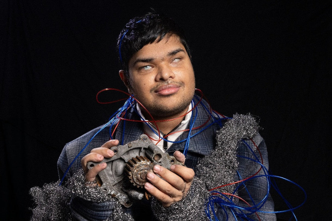 A young male holding a gadget, with red and blue ropes around his upper body