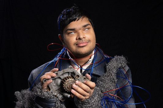 A young male holding a gadget, with red and blue ropes around his upper body