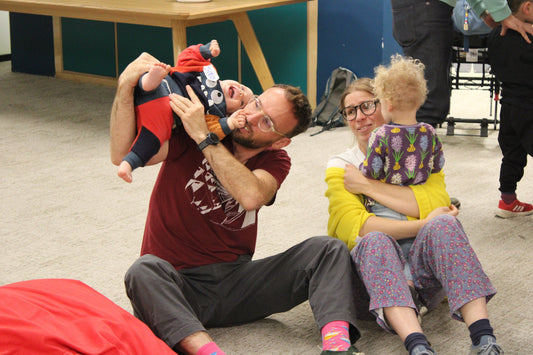 A man holds his baby on his shoulder, playing, while a woman sits next to him with her arms around a young child.