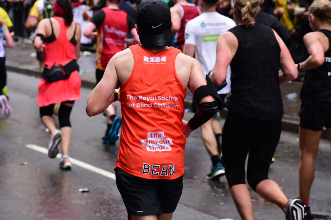 An RSBC marathon runner during the race. The image is taken from behind, and he's wearing a red RSBC vest with 'BEAN' across the bottom and a black skip cap.