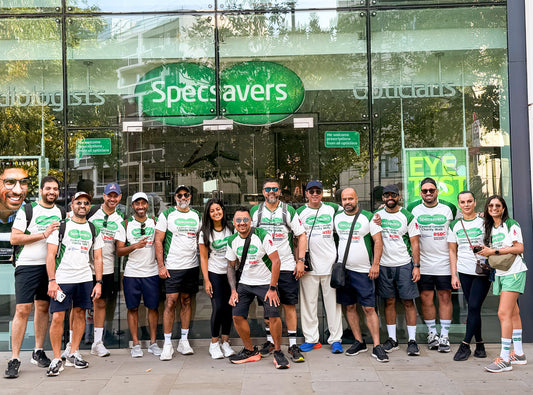 Group of 14 people in matching Specsavers branded green and white shirts standing in-front of a Specsavers store.