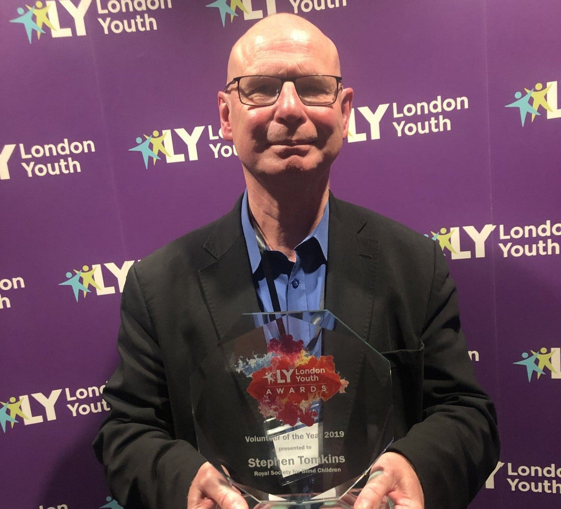 Steve, dressed in a blue shirt and black blazer holding a Volunteer of The Year award in front of a London Youth branded backdrop.