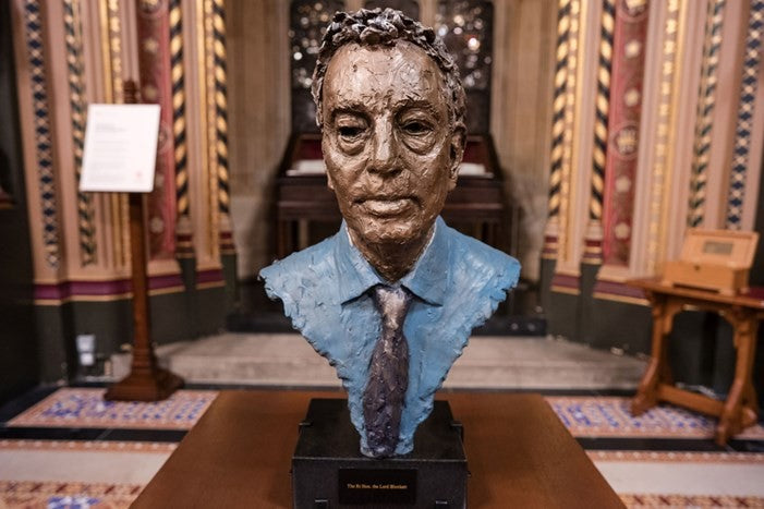 Lord David Blunkett bust in situ at the House of Lords. Placed on a table with an ornate backdrop. The bust is head and partial shoulders wearing a collar and tie.