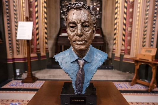 Lord David Blunkett bust in situ at the House of Lords. Placed on a table with an ornate backdrop. The bust is head and partial shoulders wearing a collar and tie.