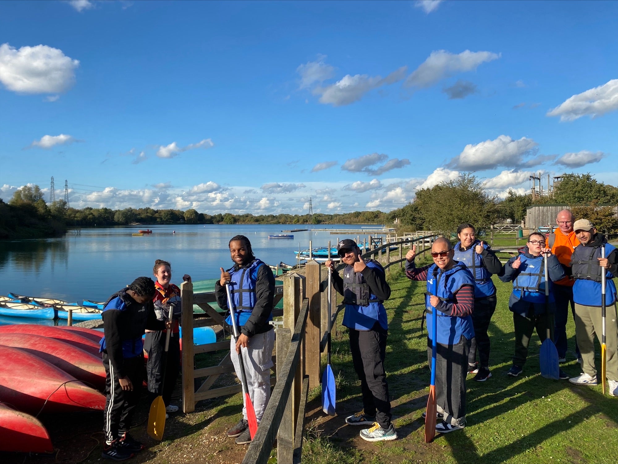 a group of happy young people in lifejackets ready to go kayaking on a lake in glorious sunshine