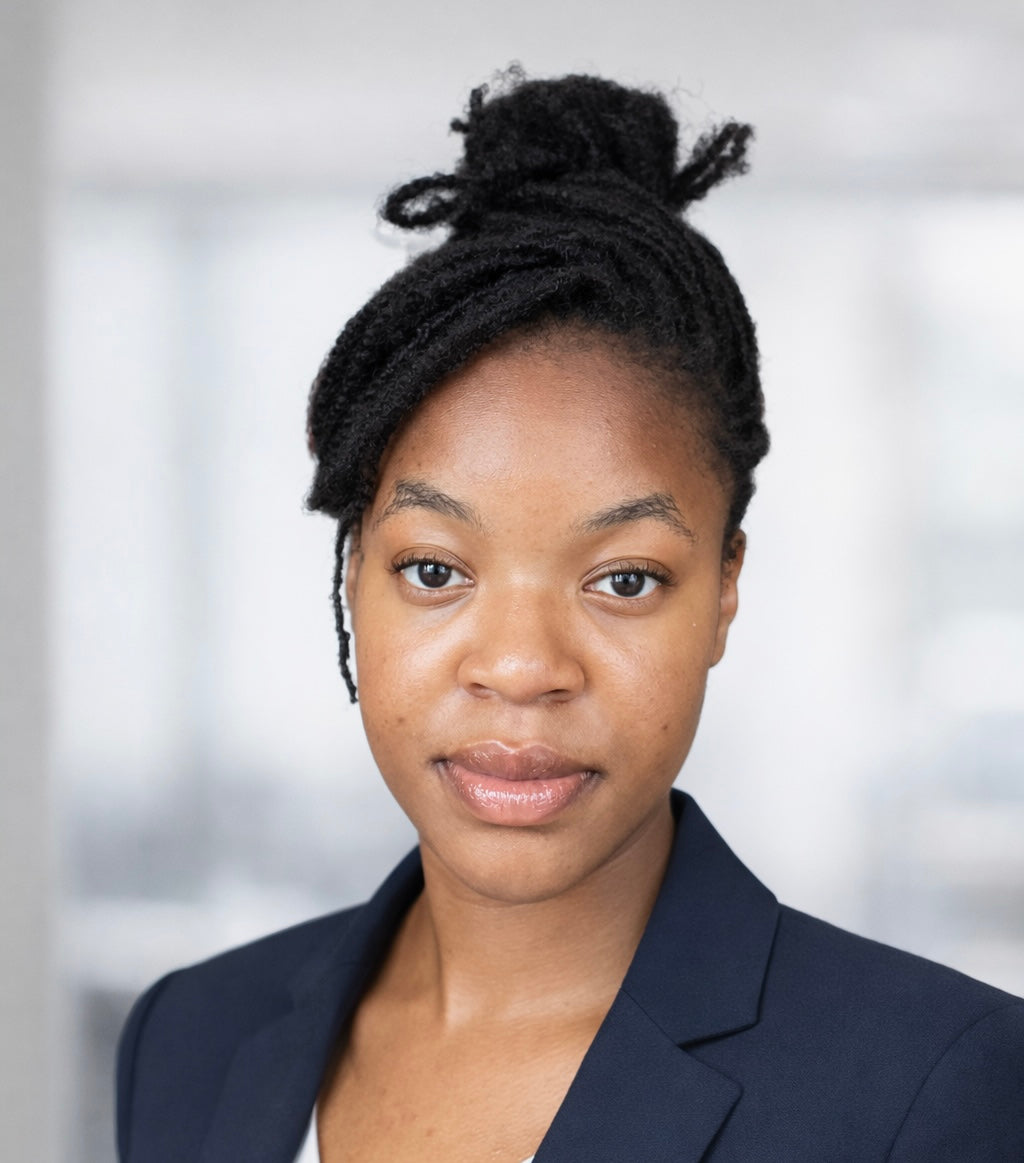 Alicia, a woman with dark braided hair styled in a bun wearing a navy blazer against a softly blurred background.