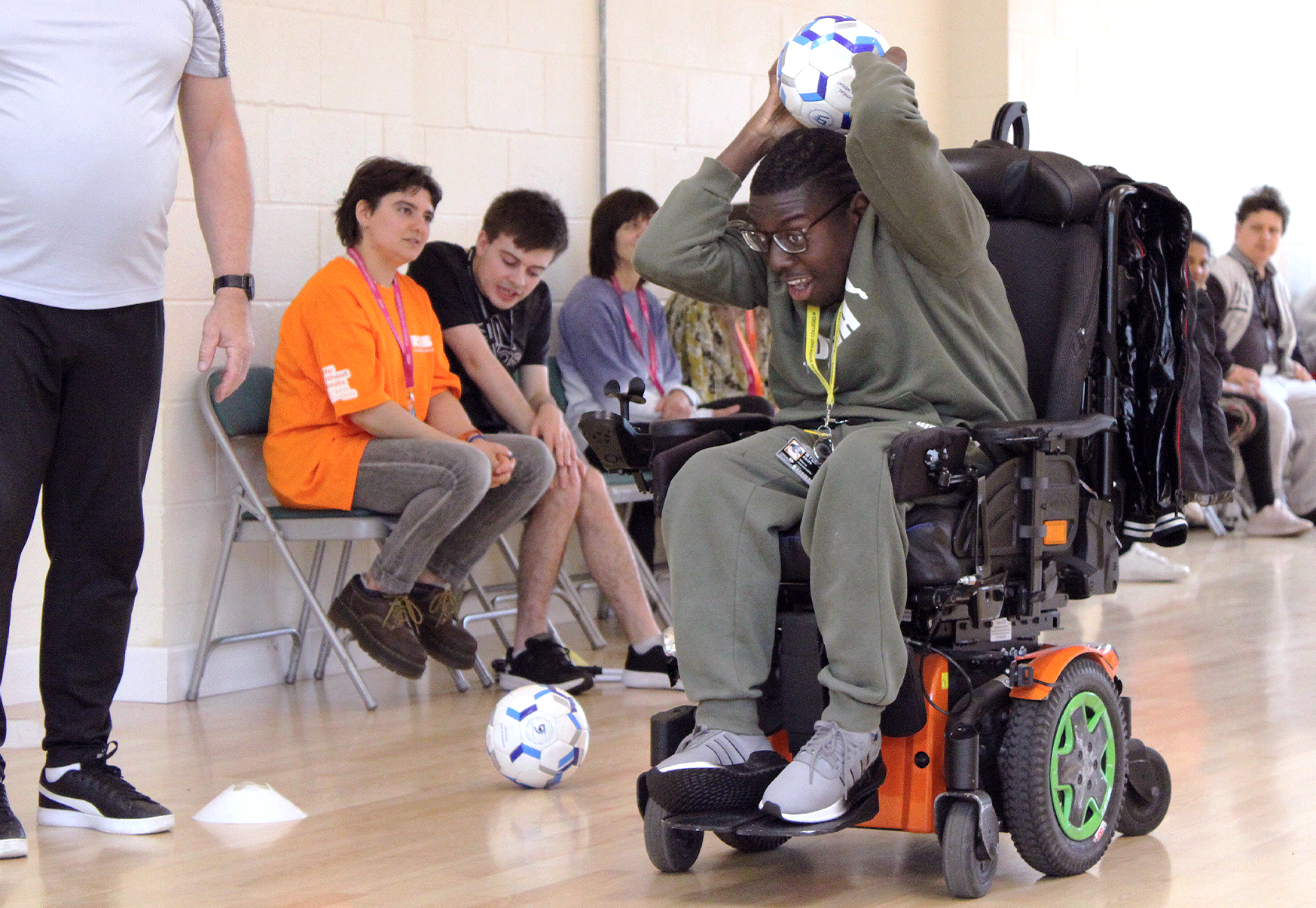 A young man in a wheelchair throwing a football over his head, with people watching behind him