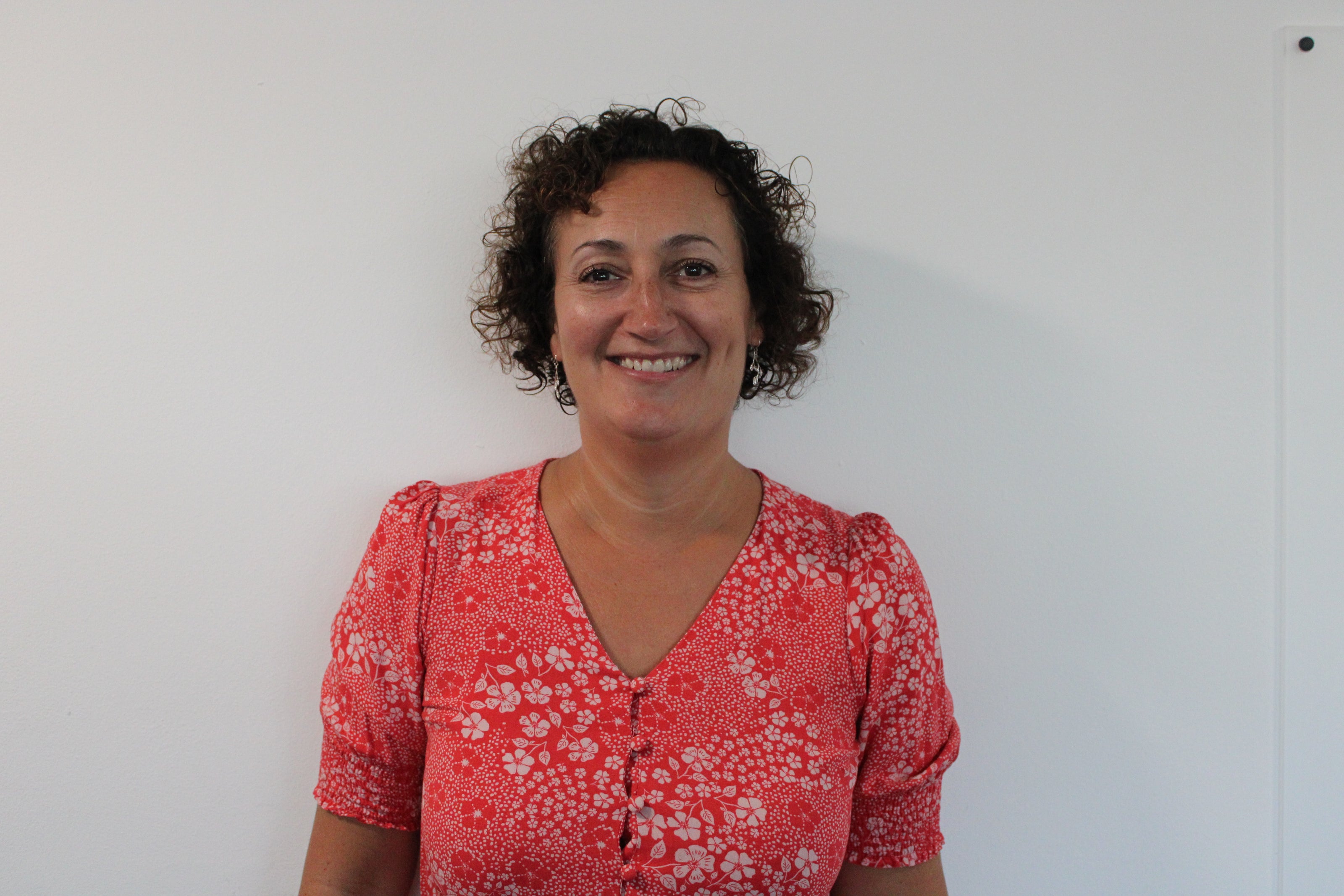 Anne-Marie, a woman wearing a red floral blouse against a white background