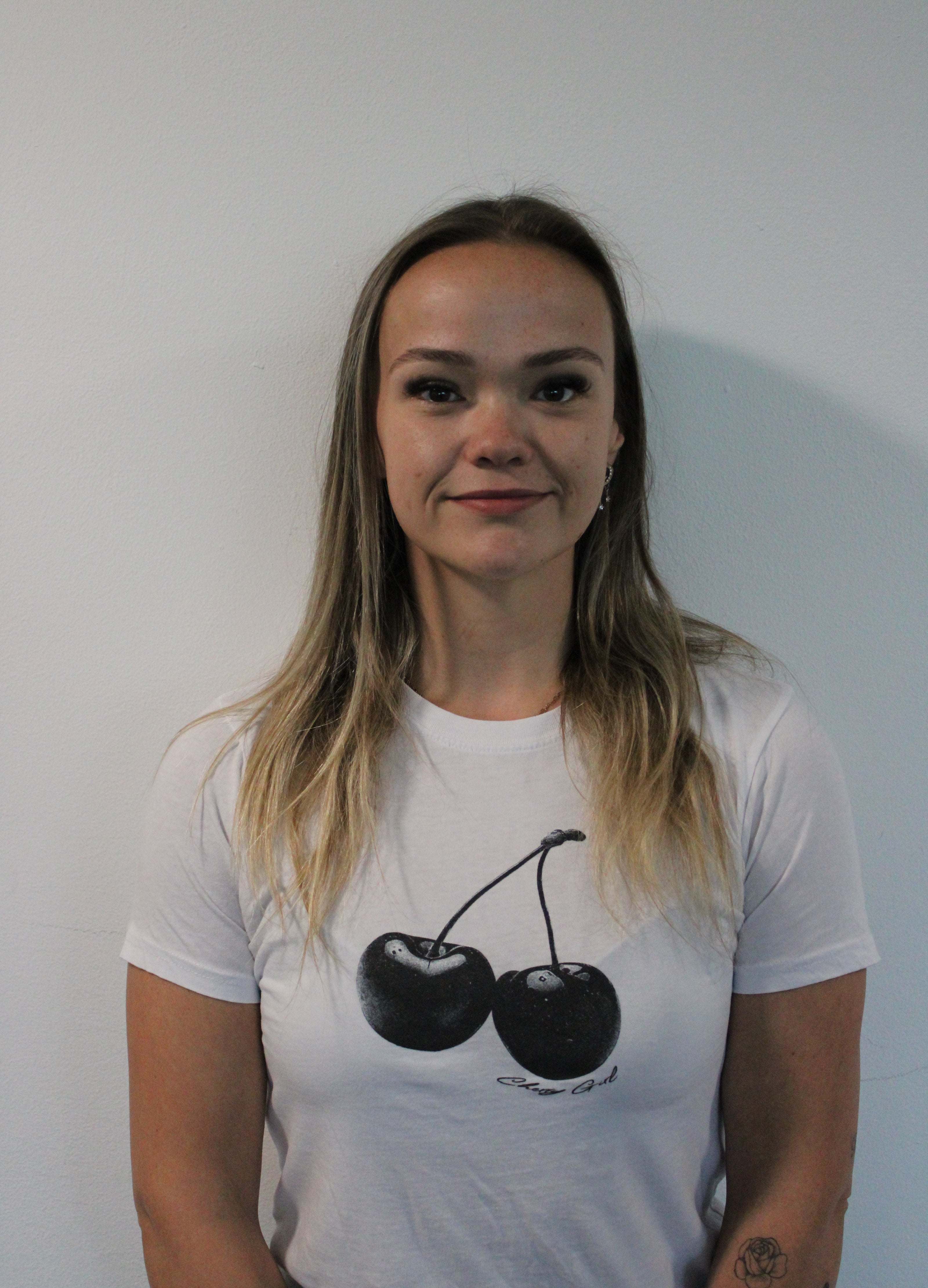 Michaela, a woman wearing a white t-shirt with black cherry design on a plain background