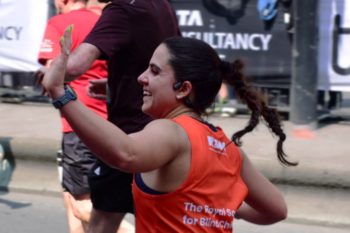 Woman in an orange running shirt celebrating a race finish with a banner in the background
