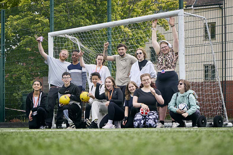 A group of adults and young people cheering in front of football goal posts