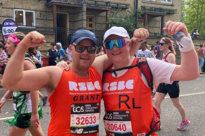 Two runners in orange vests celebrating at a race event on a street.