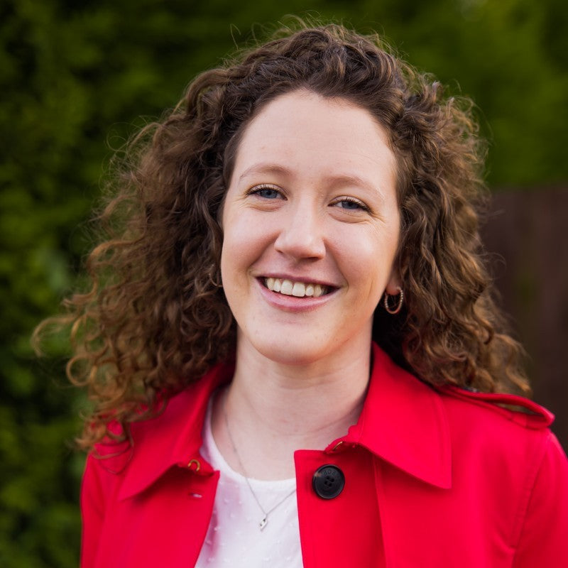Helen is a light-skinned young woman with lush dark blond curly hair, blue eyes and a bright smile. She is wearing a red jacket.