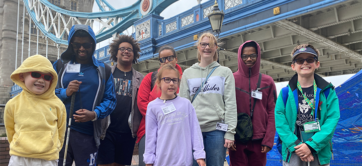 Group of smiling young people posing in front of Tower Bridge.