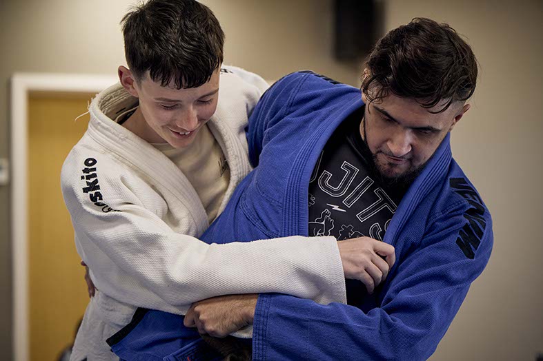 A Judo teacher indstucts a young person in a combat technique. The young persons laughs whilst gripping the teacher.