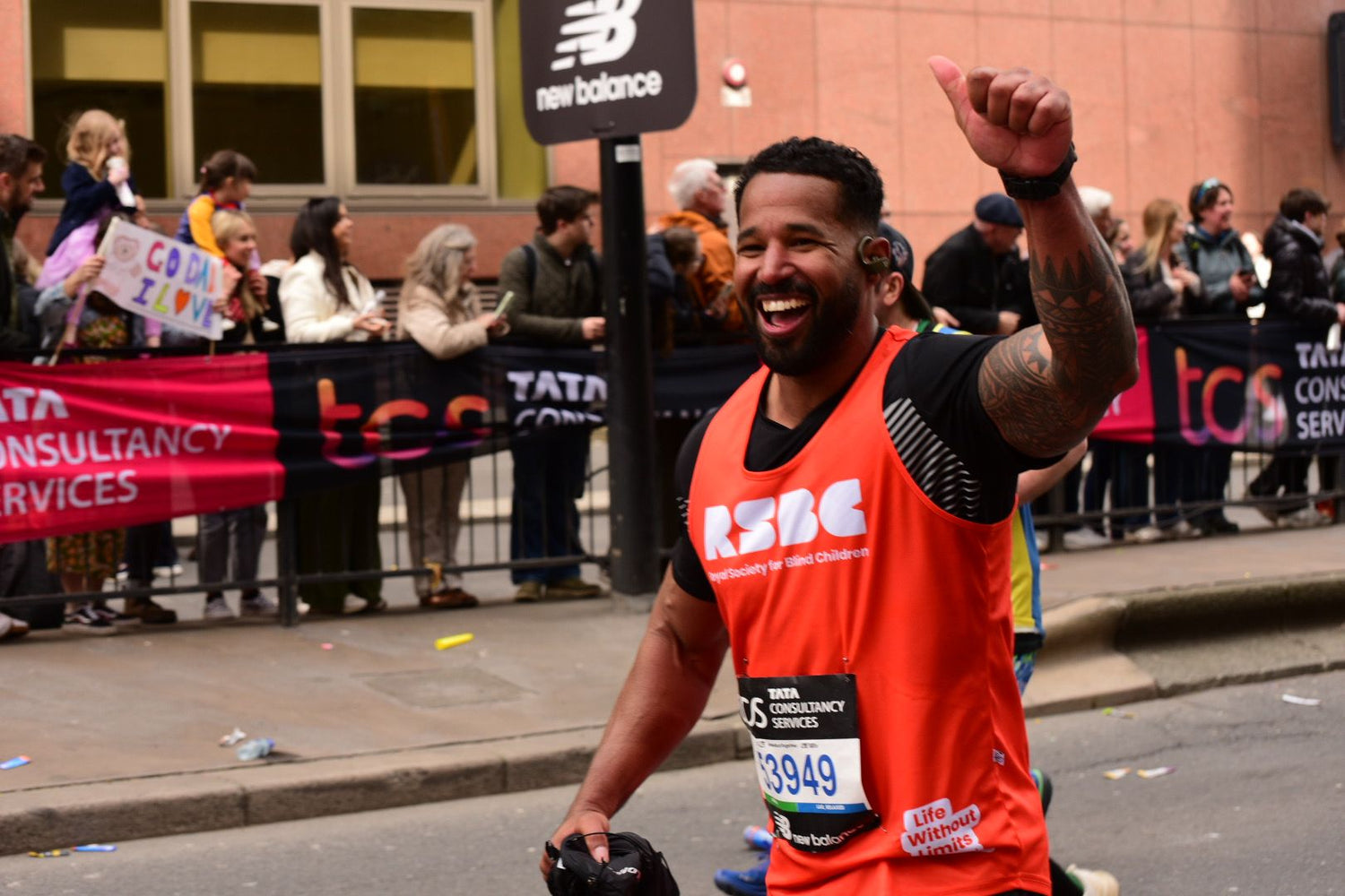 Man in an orange RSBC running vest and New Balance top underneath, celebrating whilst running the London Marathon.