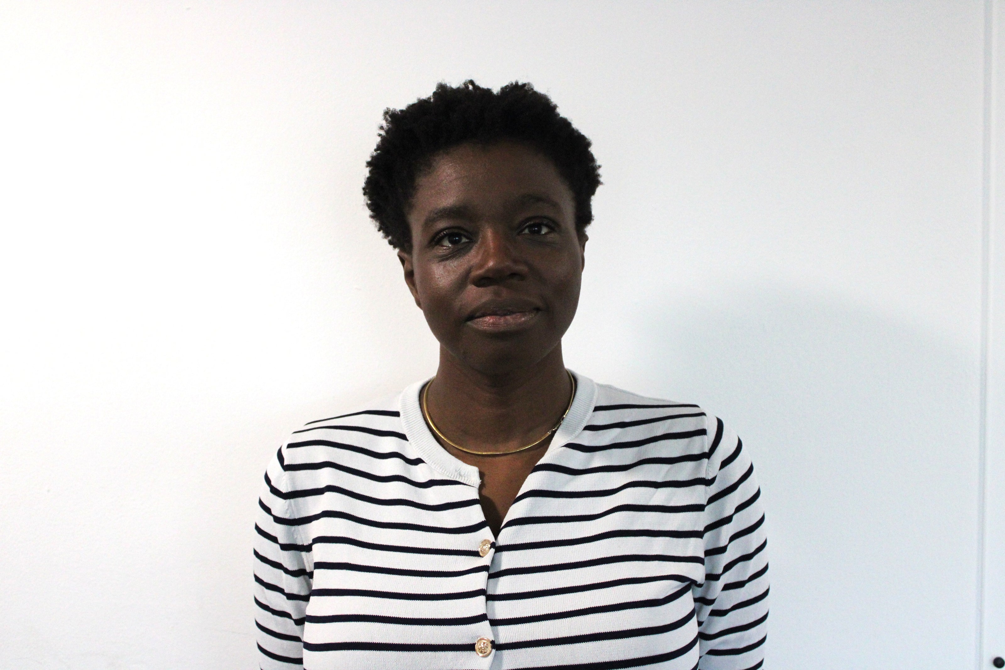 Lola, a woman wearing a white shirt with black horizontal stripes standing against a plain white background.
