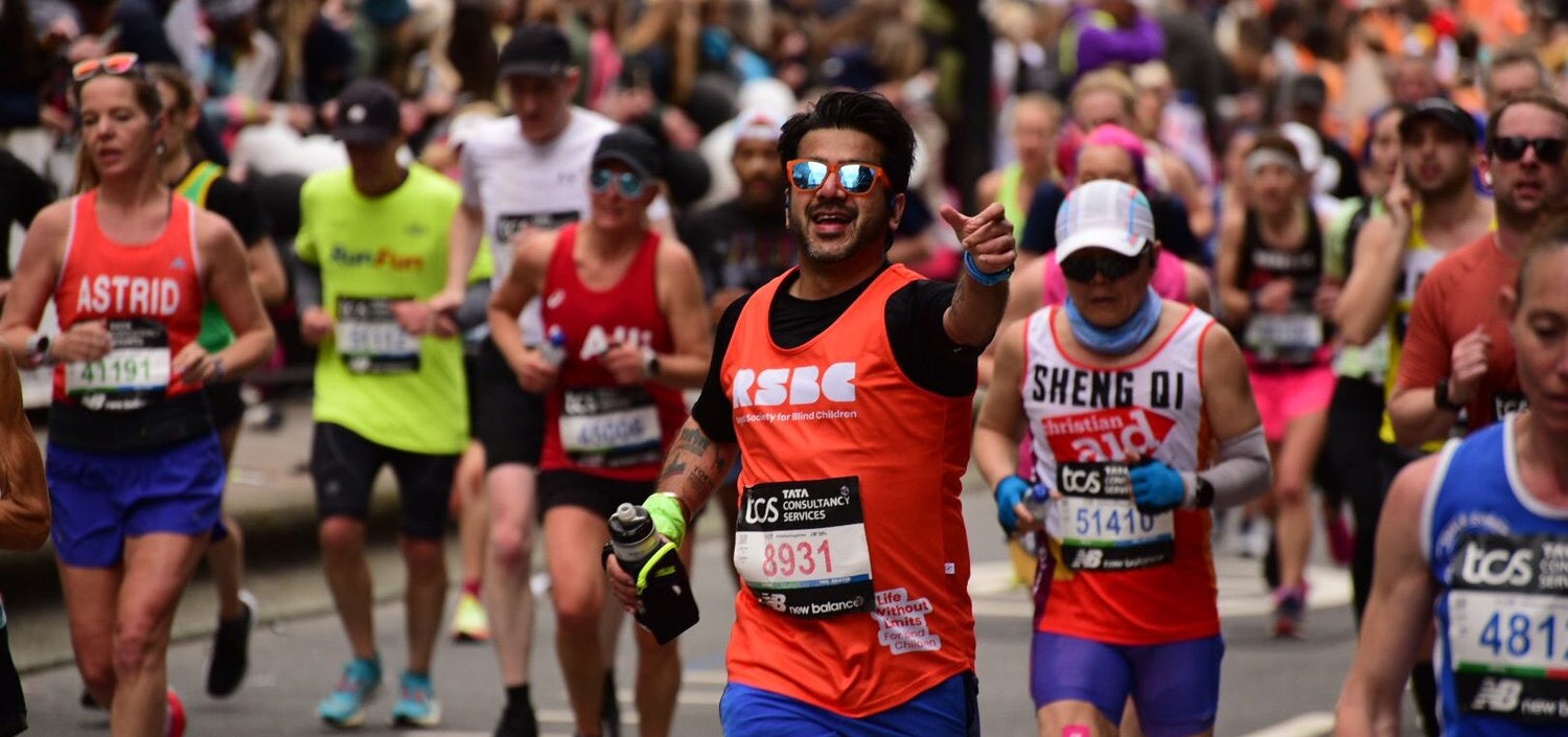 Marathon runners in orange RSBC vest racing towards the camera with reaching hand, crowds in the background.