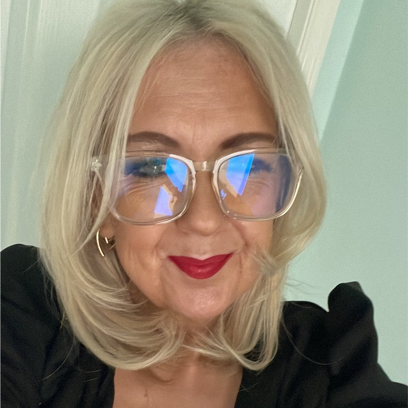 A smiling blonde lady with gold glasses and bright red lipstick