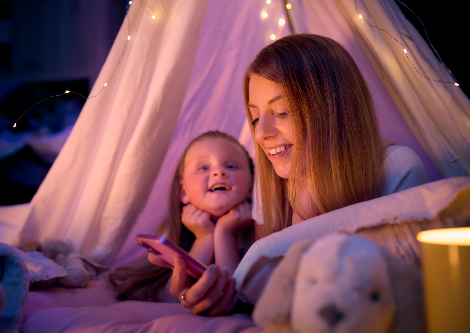 Mother and child in a cozy indoor setting with a pink canopy and string lights.