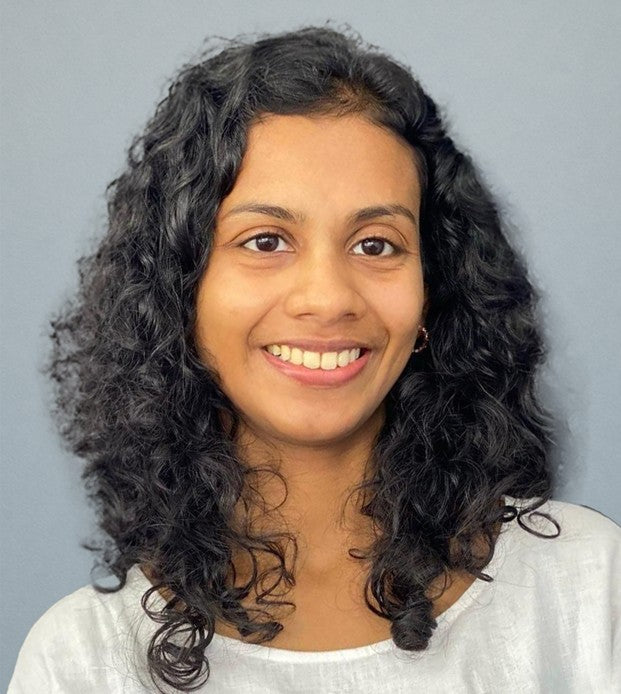 Woman with curly hair smiling against a plain light blue background.