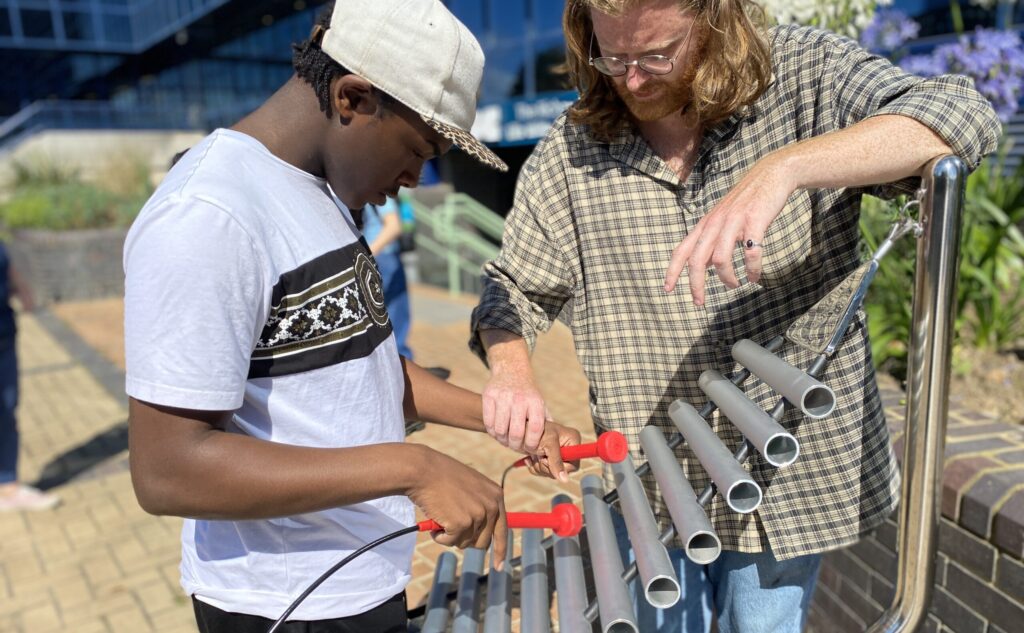 Young man and man playing metal instrument outdoors.