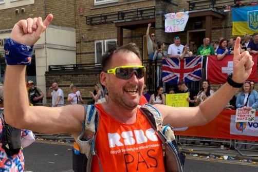 Man in an orange vest celebrating in a marathon with spectators and flags in the background.