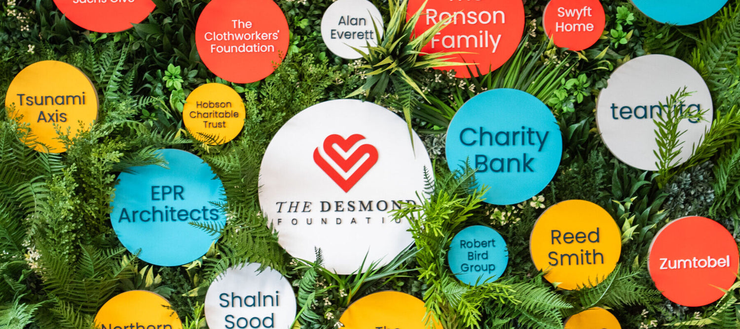 Coloruful circular logos of various organisations arranged on green foliage, featuring The Desmond Foundation prominently in the center.