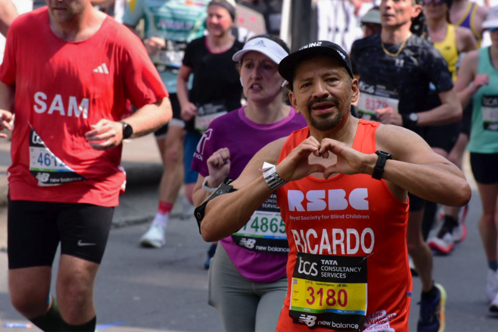 Runner in an orange RSBC shirt making a heart shape with his hands during the London Marathon 2025.