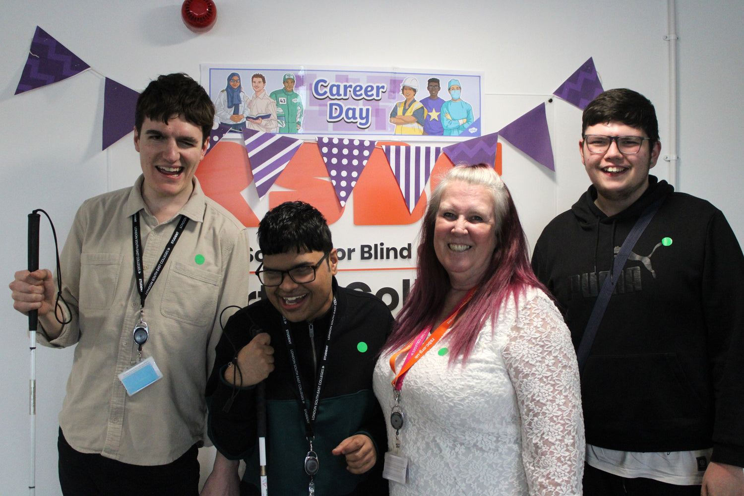 Four people posing together in front of a 'Career Day' banner with purple flags.