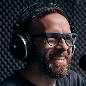 A man with a beard and glasses in a recording studio with headphones smiling