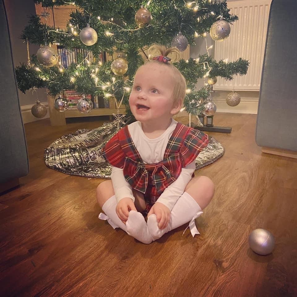 A little girl sat in front of a Christmas tree