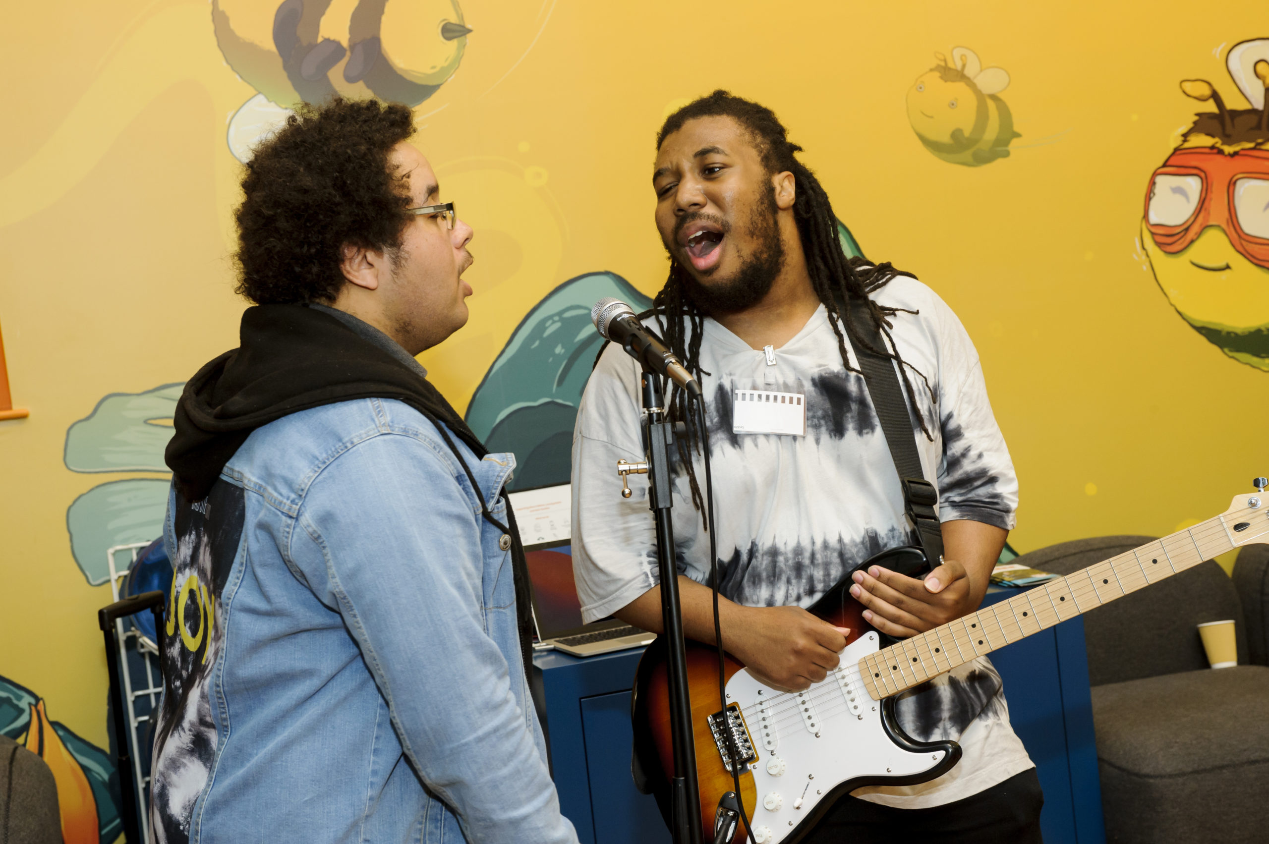 Two young men performing a song, one is singing and one is playing the guitar