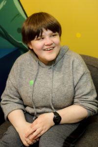 A young woman is sitting on a chair looking to her right and smiling