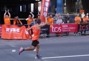 A RSBC runner waving at people standing up at the RSBC cheer point 