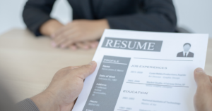 Two hands holding a resume with someone crossing his hand in the background