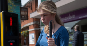 A young woman at a traffic light holding a cane