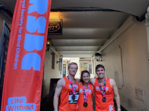 A group of 3 runners smiling wearing a medal each next to a RSBC Banner