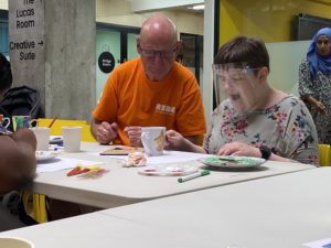 A young woman doing ceramics decoration next to a man wearing a RSBC volunteer t-shirt